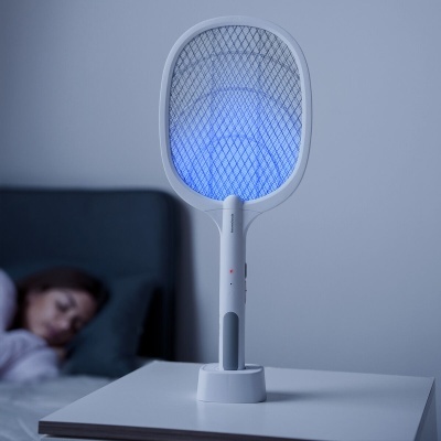 Racquete elétrica branca com luz azul numa mesa ao lado de pessoa a dormir