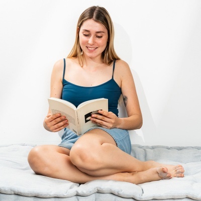 Mulher jovem sentada lendo livro com top azul e saia jeans