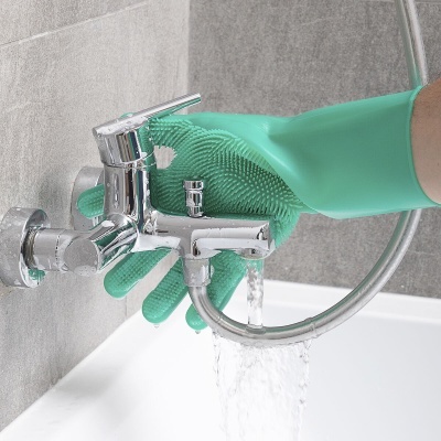 Luva verde de silicone a segurar torneira cromada com água a correr