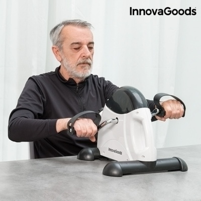 Mini bicicleta estática InnovaGoods branca e preta sobre mesa cinzenta com homem a usar
