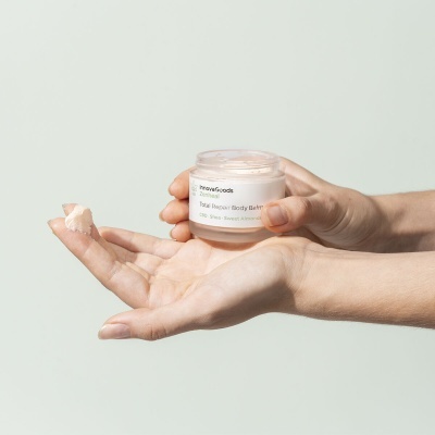 Frasco de creme corporal InnovaGoods Total Repair Body Butter e mãos aplicando creme