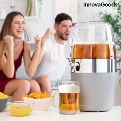 Dispensador de bebida cinza e prata com cerveja e caneco de vidro ao lado de tigelas de snacks, pessoas sorrindo ao fundo.