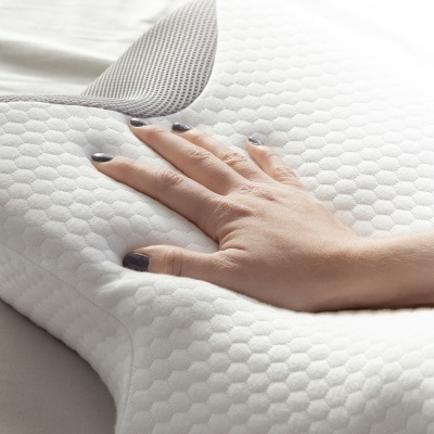 Travesseiro branco com textura hexagonal e painel cinza de malha sendo pressionado por uma mão