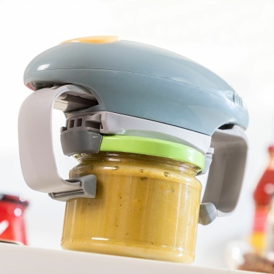 Abridor manual de frascos em plástico cinza, branco e verde a abrir frasco de vidro com tampa verde e creme amarelo.