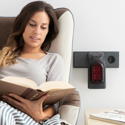 mulher sentada a ler em poltrona com sensor preto com luzes vermelhas numa tomada na parede ao lado