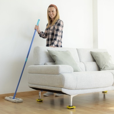 Mulher a limpar chão de madeira clara com esfregão azul junto a sofá cinzento