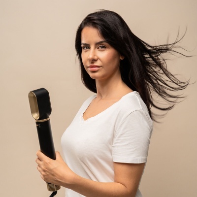 Mulher com cabelo preto segurando aparelho de estilização capilar preto e dourado.