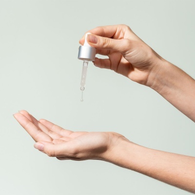 Mãos segurando doseador deixando cair gota de líquido na palma