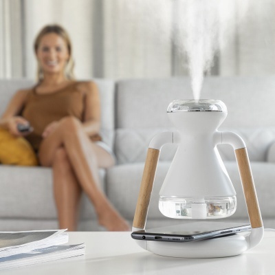 Humidificador branco com detalhes em madeira a emitir vapor numa mesa ao lado de um telemóvel