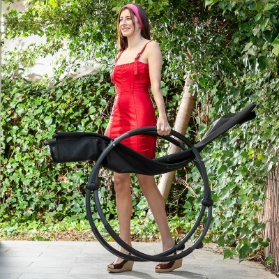 Mulher com vestido vermelho segura berço portátil preto em ambiente exterior com vegetação