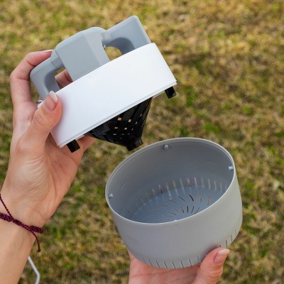 Aparelho elétrico portátil cinza e branco desmontado com relvado ao fundo