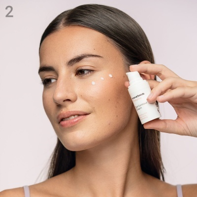 Mulher aplicando creme no rosto com recipiente branco pequeno