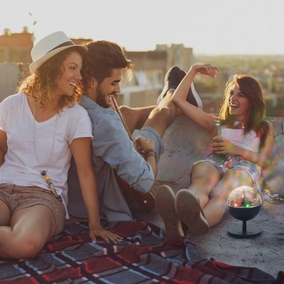 Três jovens sentados no terraço ao pôr do sol com guitarra, chapéu branco, roupa casual e luz de discoteca