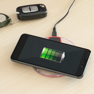 Smartphone preto a carregar sobre base sem fios vermelha e transparente ao lado de comando de carro preto