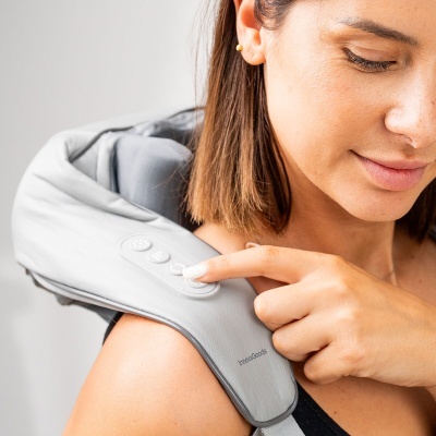 Pessoa com máquina massageadora cinza claro no ombro e pescoço, mão a carregar botão.