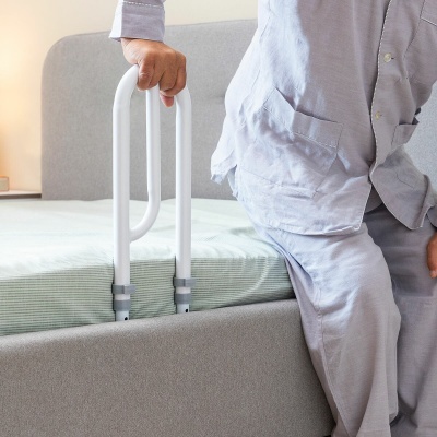 Pessoa sentada numa cama segurando barra de apoio branca