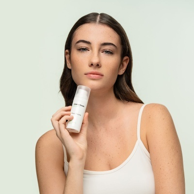 Mulher a segurar frasco branco com tampa prateada em fundo claro