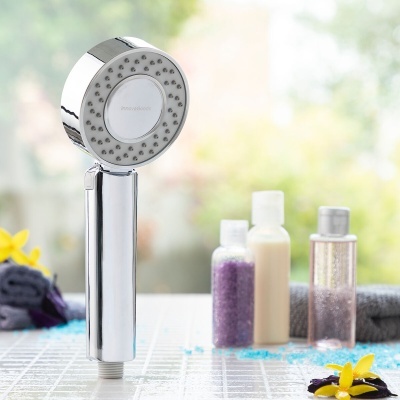 Chuveiro de mão cromado com borrifadores cinza e três frascos com líquidos e sais coloridos em fundo desfocado