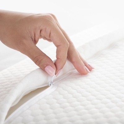 Mão feminina a abrir fecho branco em colchão ou protetor branco com padrão hexagonal.