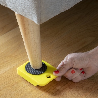 Suporte amarelo para mover móveis sob perna de madeira clara de móvel estofado cinza em chão de madeira clara