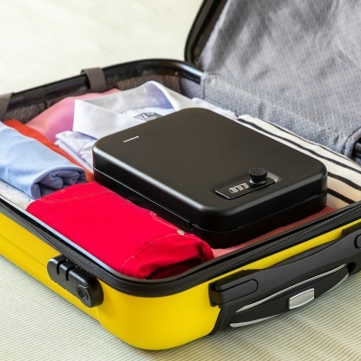 Mala de viagem amarela aberta com roupas e uma caixa preta com fechadura