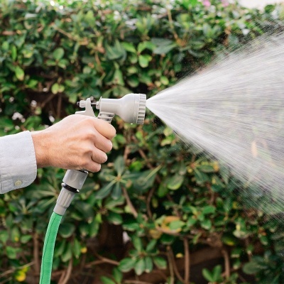 Mão com pistola de pulverização a jorrar água em jardim com folhagem