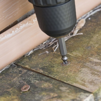 Broca preta de parafusadeira a fixar parafuso em madeira escura junto a rodapé