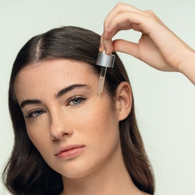 Mulher a aplicar sérum facial com conta-gotas prateado