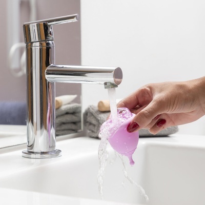 Torneira cromada a correr água com copo menstrual rosa a ser lavado