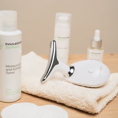 Dispositivo de cuidados faciais com três frascos de produtos e toalha sobre mesa de madeira