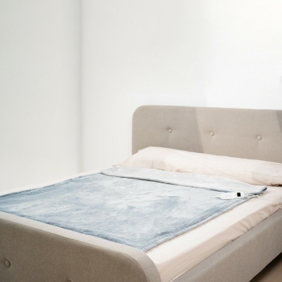 Cama estofada cinza claro com colcha azul clara e parede branca ao fundo