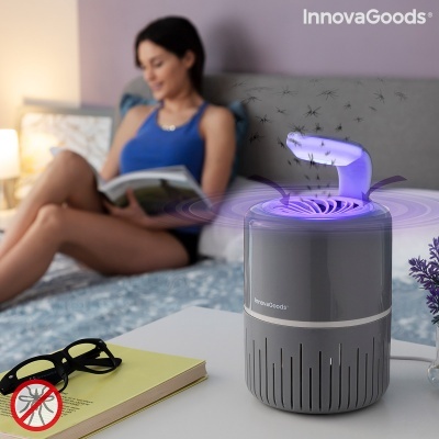 Mosquito elétrico cinza InnovaGoods em mesa branca com luz púrpura, mulher lendo ao fundo