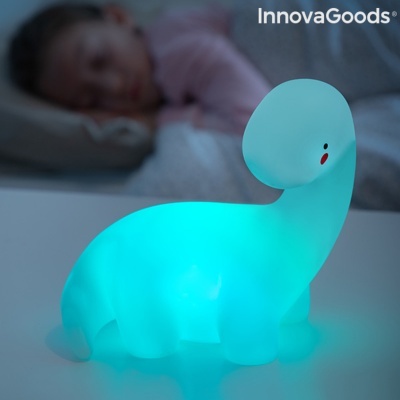 Lâmpada de dinossauro azul iluminada numa mesa branca com criança ao fundo