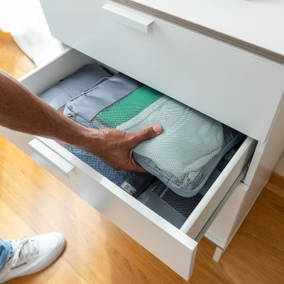 Sacos organizadores cinzentos em gaveta branca cheia com roupas dobradas