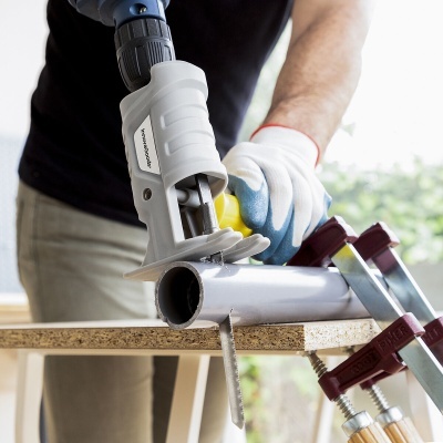 Pessoa a usar máquina elétrica WORX para cortar tubo fixado com grampos numa bancada de madeira