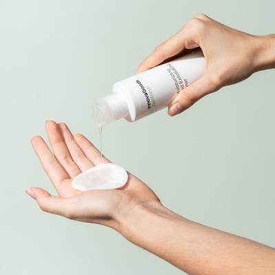 Frasco branco a despejar líquido transparente sobre disco de algodão em mãos