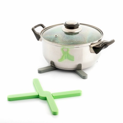 Panela de aço inoxidável com tampa de vidro e pegas pretas em cima de base verde em forma de cruz