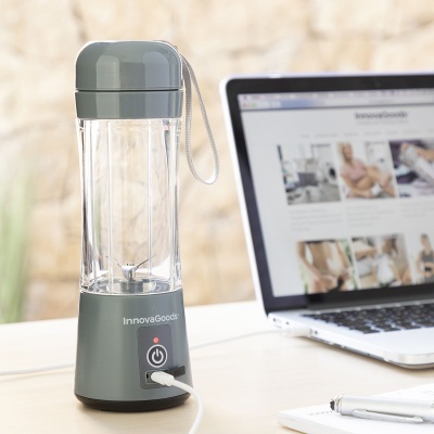 Liquidificador portátil cinzento e transparente da InnovaGoods numa mesa ao lado de um portátil