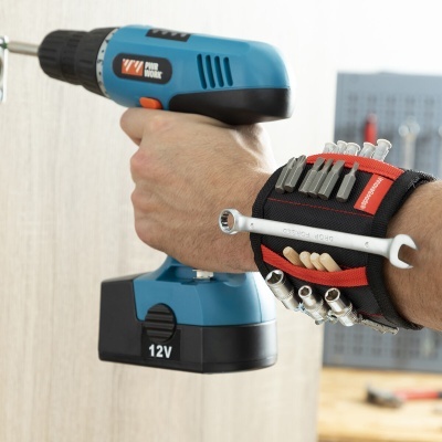 Pessoa a usar furadeira/parafusadora azul e preta com pulseira magnética preta e vermelha cheia de ferramentas pequenas.