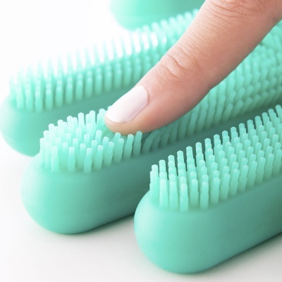 Escova de silicone azul claro com cerdas flexíveis e dedo a pressionar uma cerda.