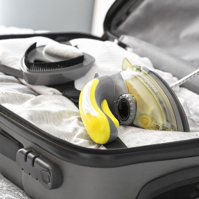 Mala de viagem aberta com ferro a vapor amarelo e escova preta sobre roupa branca