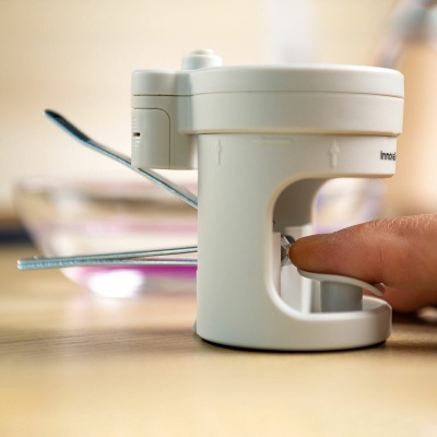 Dispositivo manual branco com hastes metálicas numa mesa de madeira