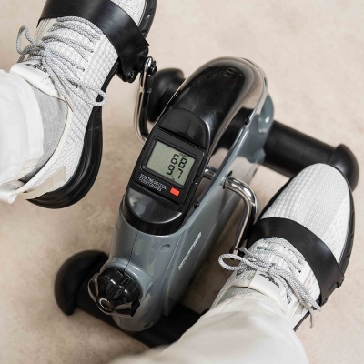 Pedalinho de exercício cinzento com monitor digital em uso com calçado desportivo branco
