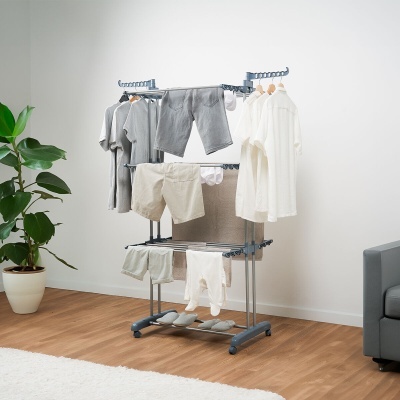 Estendal metálico com roupas penduradas numa sala com planta e sofá.