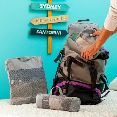 Mochila cinzenta aberta com bolsas de rede e placa de destinos colorida na parede azul