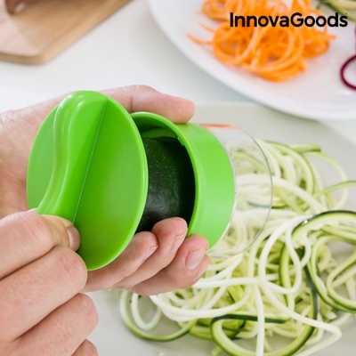 Suporte verde para fatiar vegetais em espiral com abobrinha e fatias ao fundo.