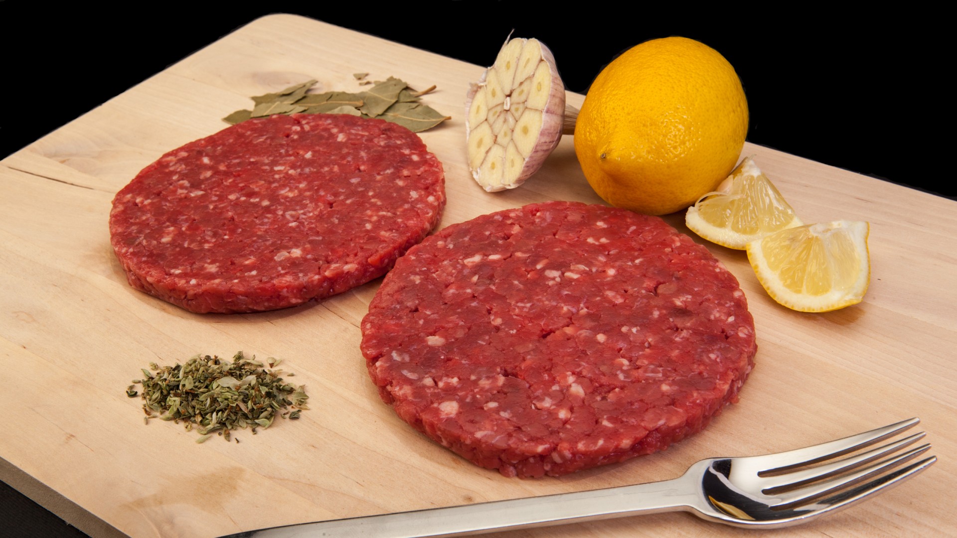Hambúrguer de Vaca 200g Hambúrgueres crus com alho, limão e ervas numa tábua de madeira