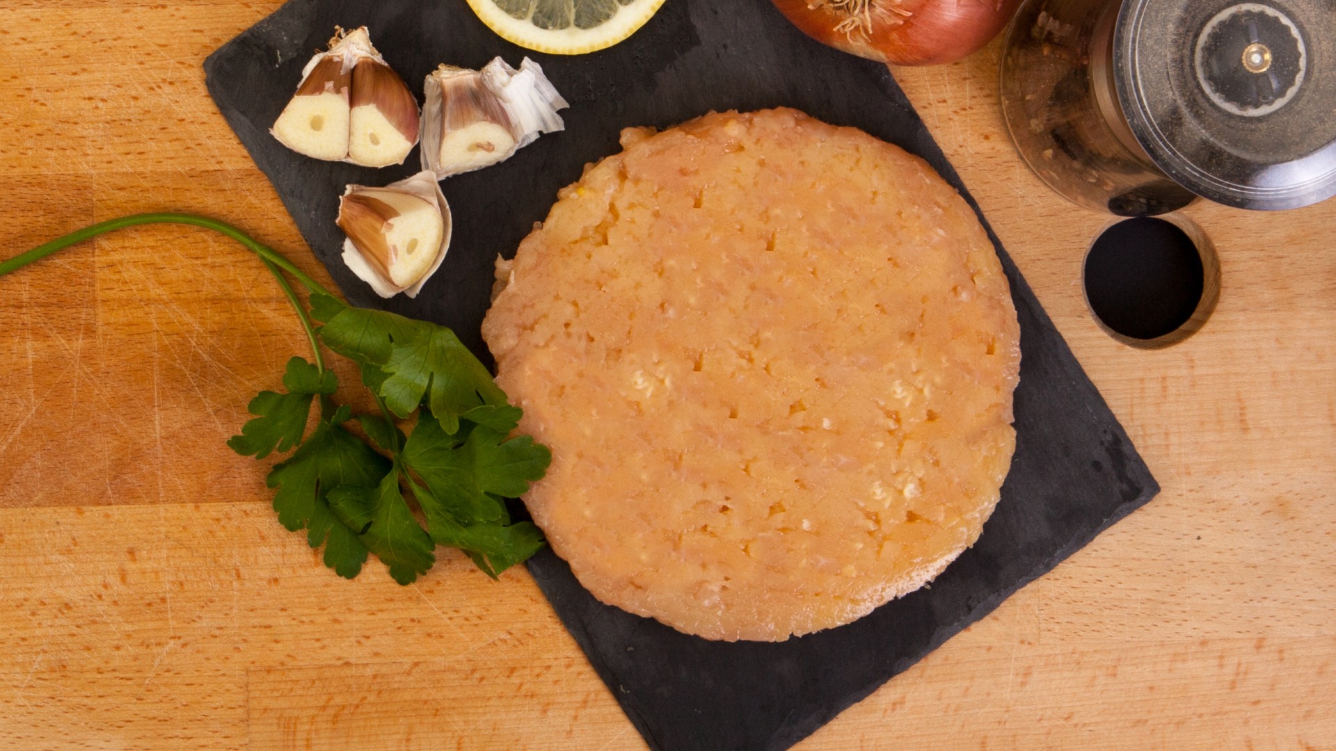 Hambúrguer de Frango do Campo 200g. Hambúrguer de carne crua com alho, limão e cebola numa tábua de ardósia sobre madeira