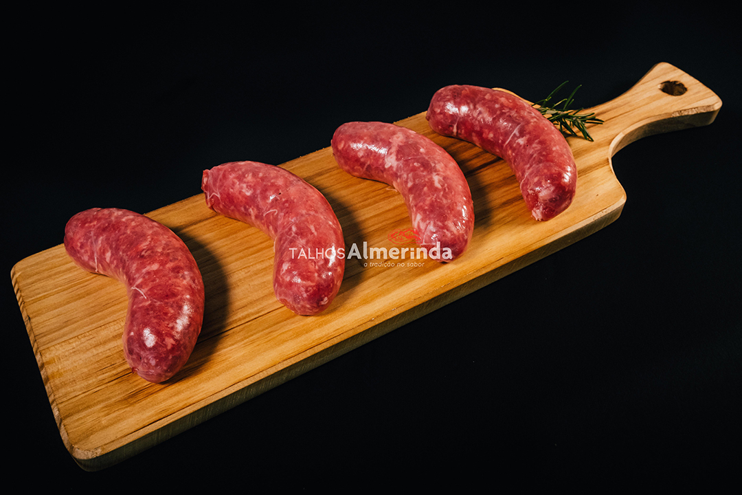 Salsicha Brasileira Quatro salsichas cruas numa tábua de madeira clara sobre fundo preto