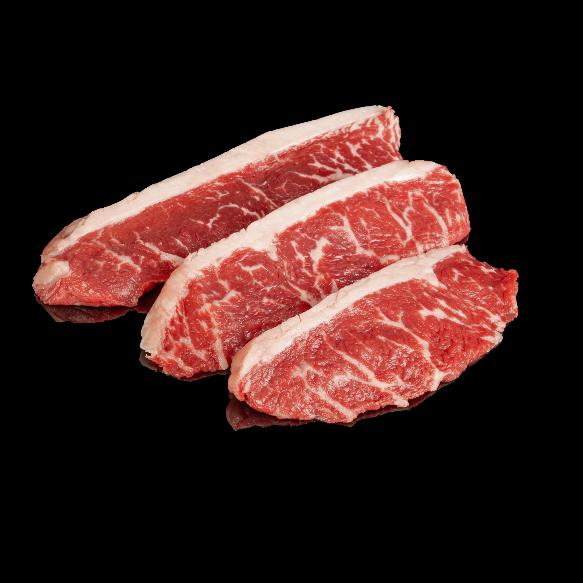 Picanha Angus Três bifes crus de carne vermelha com marmoreio branco em fundo preto